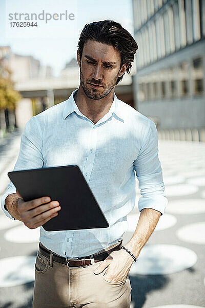 Businessman with hand in pocket using tablet PC on sunny day