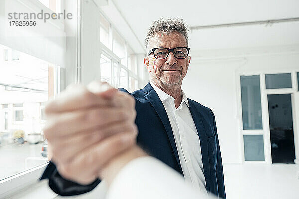 Lächelnder Geschäftsmann hält die Hand seines Kollegen am Arbeitsplatz