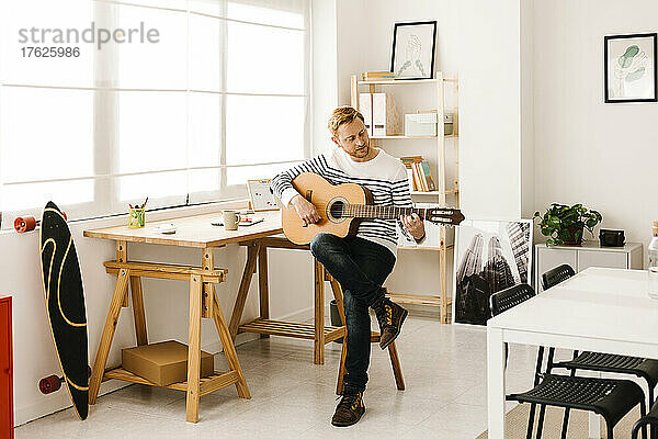 Mann übt Gitarre im heimischen Wohnzimmer
