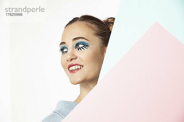 Lächelnde Frau mit kreativem Augen-Make-up vor weißem Hintergrund