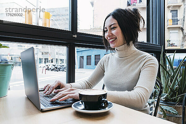 Glückliche Geschäftsfrau  die im Café einen Laptop benutzt