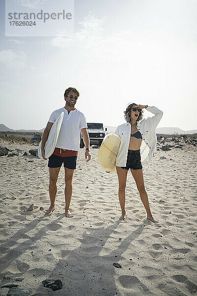 Glückliches Paar steht an einem sonnigen Tag mit Surfbrett am Strand