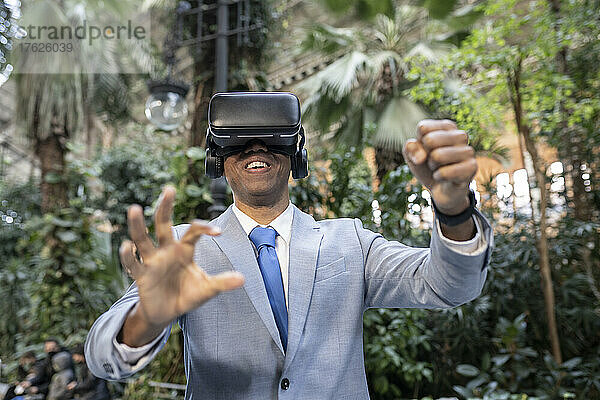 Lächelnder Geschäftsmann mit Virtual-Reality-Simulator gestikuliert vor Pflanzen