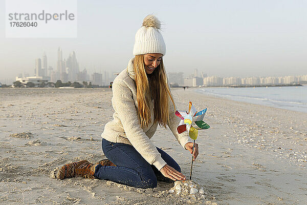 Glückliche Frau sitzt auf Sand mit buntem Windradspielzeug am Strand