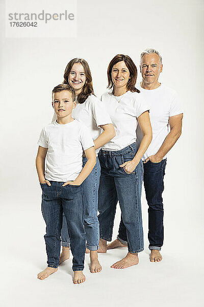 Junge mit Eltern und Schwester  die Hände in den Taschen vor weißem Hintergrund stehen
