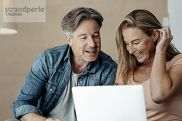 Cheerful couple using laptop at home