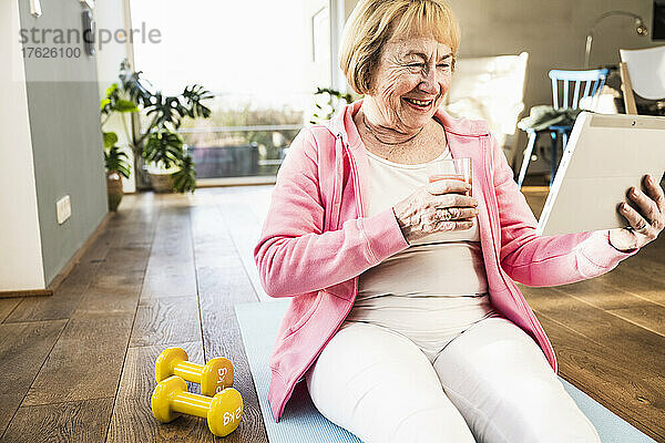 Glückliche ältere Frau mit einem Glas Saft und einem Tablet-PC zu Hause