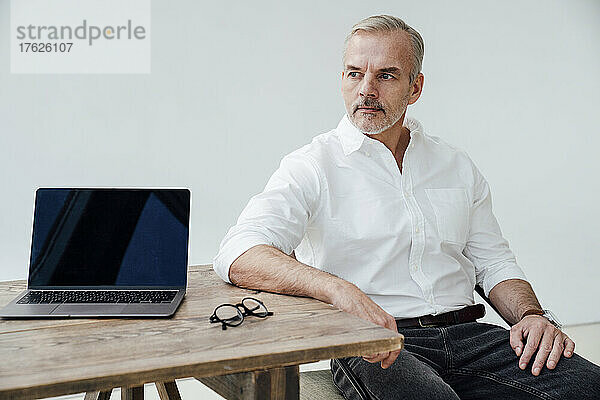 Nachdenklicher Geschäftsmann mit Laptop auf dem Schreibtisch im Büro