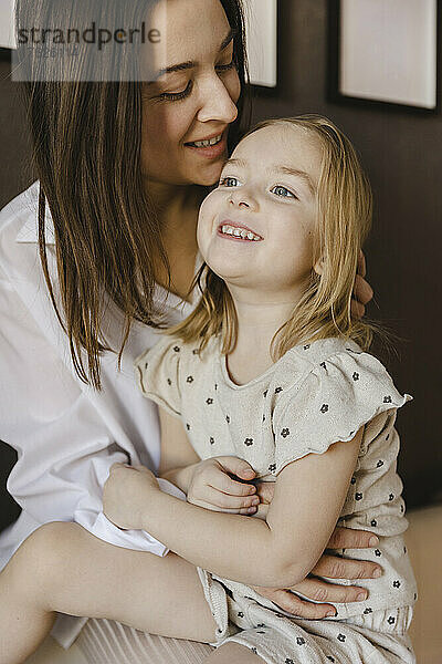 Lächelnde Frau sitzt mit süßer Tochter zu Hause