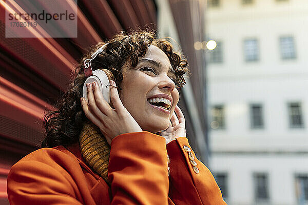Fröhliche Frau hört Musik über Kopfhörer in der Nähe der Wand