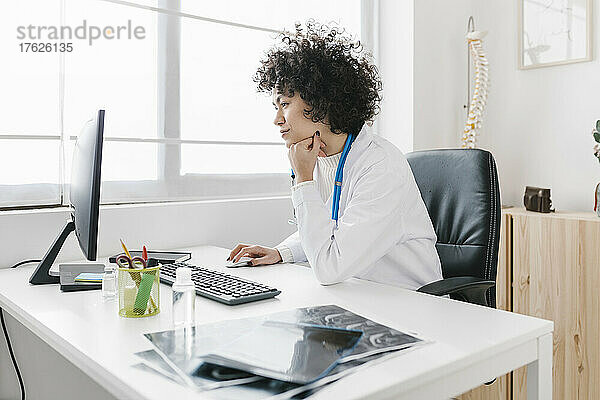 Arzt sitzt mit der Hand am Kinn und benutzt den Computer in der medizinischen Klinik