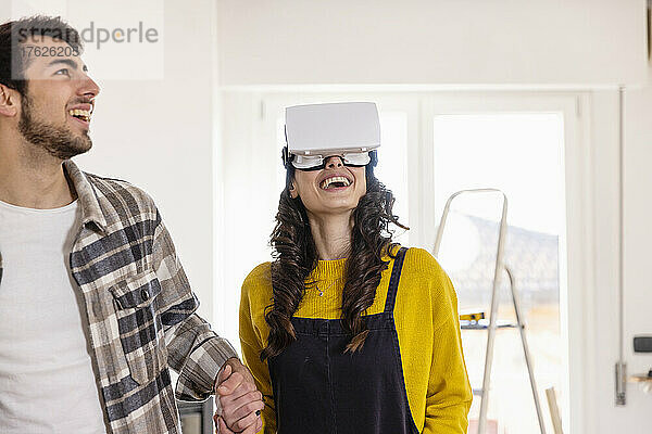 Happy woman with VR glasses holding hand of boyfriend at new home