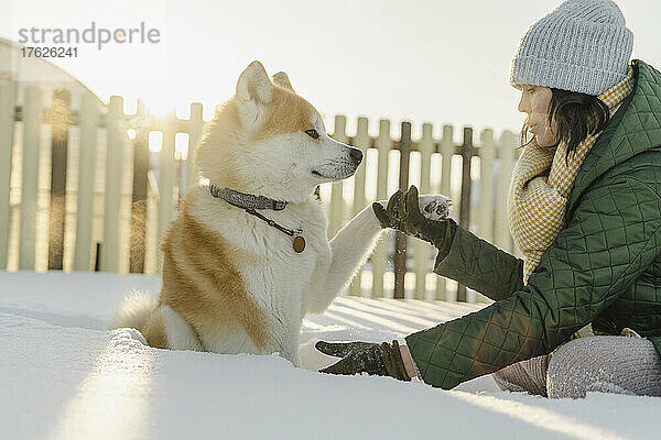 Woman holding dog paw sitting on deep snow in winter