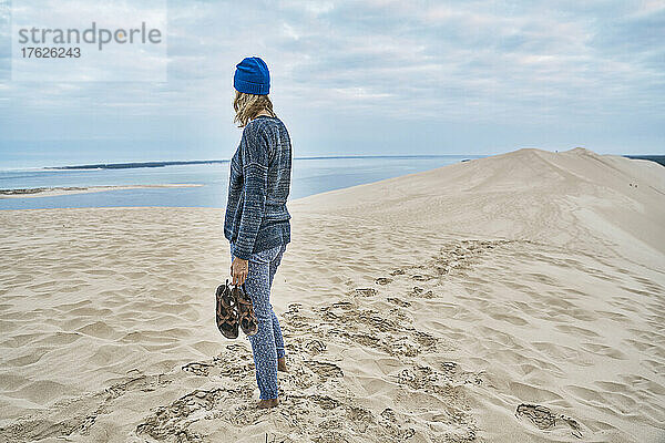 Frau mit Sandalen steht auf Sanddüne am Strand
