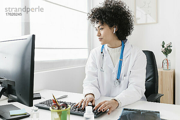 Arzt trägt In-Ear-Kopfhörer am Desktop-PC in einer medizinischen Klinik