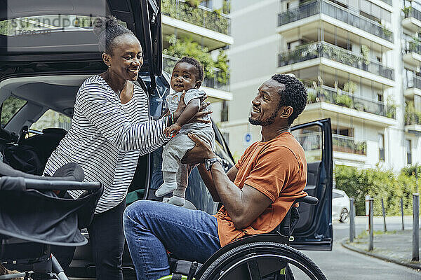 Mutter gibt ihrem im Rollstuhl sitzenden Vater ihren Sohn im Auto