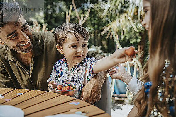 Junge teilt Erdbeeren mit seiner Schwester im Hinterhof