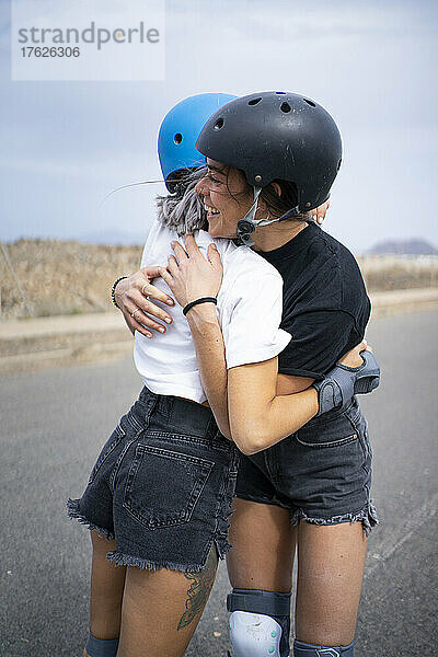 Friends wearing helmets hugging each other on road