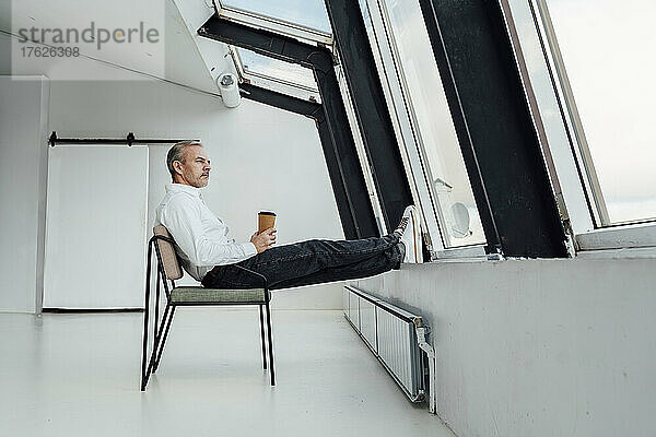 Geschäftsmann mit Einwegkaffeetasse sitzt auf Stuhl im Büro