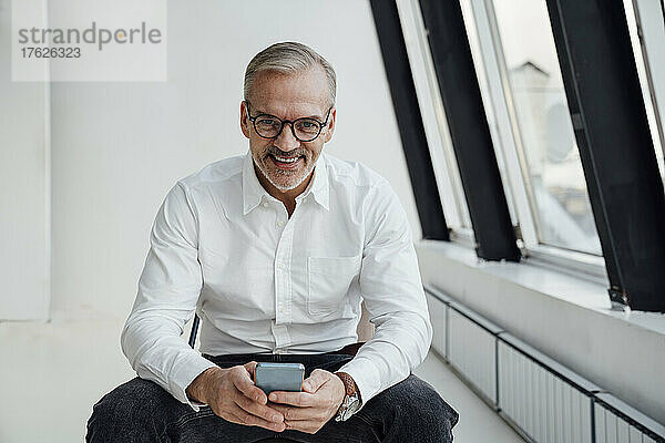 Lächelnder Geschäftsmann mit Smartphone im Büro