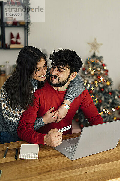 Frau umarmt ihren Freund und kauft zu Hause online über den Laptop ein