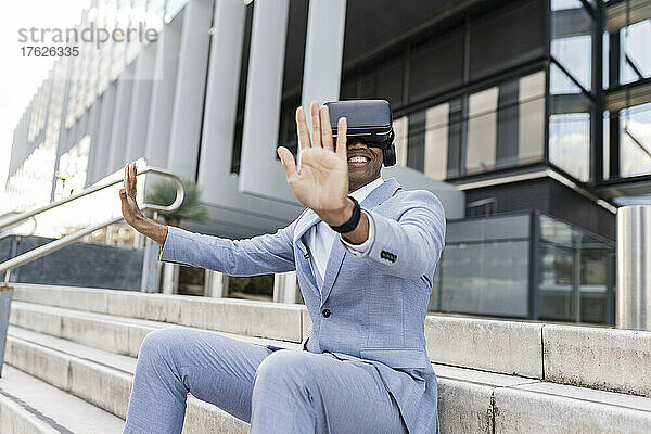 Glücklicher Geschäftsmann mit Virtual-Reality-Simulator sitzt auf Stufen