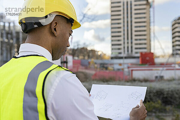 Architekt mit Schutzhelm liest Bauplan auf Baustelle