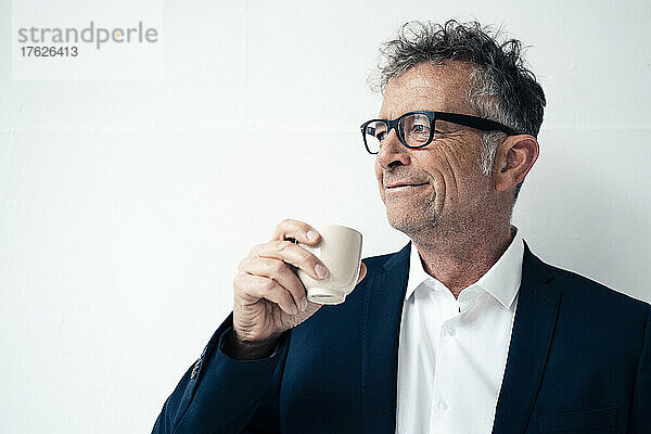 Lächelnder Geschäftsmann  der Kaffee vor weißem Hintergrund trinkt