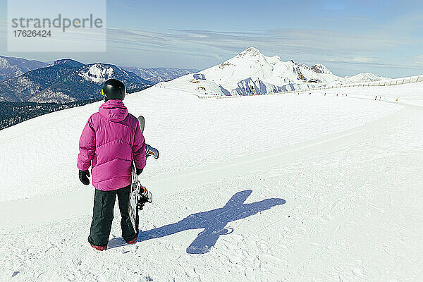 Mann mit Snowboard steht auf schneebedecktem Berg