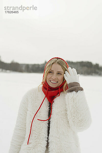 Happy blond woman wearing warm clothing standing with hand in hair