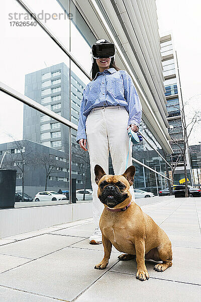 Glückliche Geschäftsfrau mit Virtual-Reality-Simulator steht mit Hund auf Fußweg