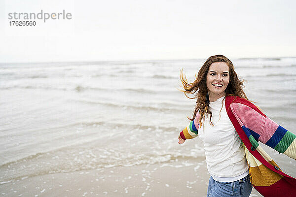 Glückliche junge Frau mit ausgestreckten Armen genießt den Strand