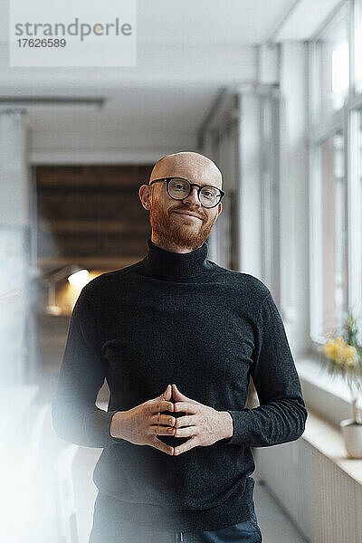 Smiling businessman with beard wearing eyeglasses standing in office
