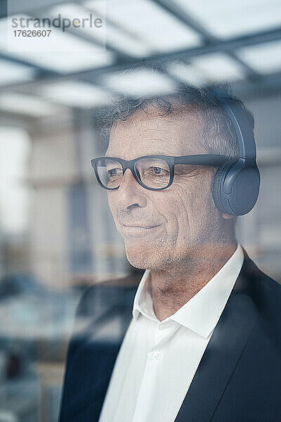 Nachdenklicher älterer Geschäftsmann mit Kopfhörern im Büro