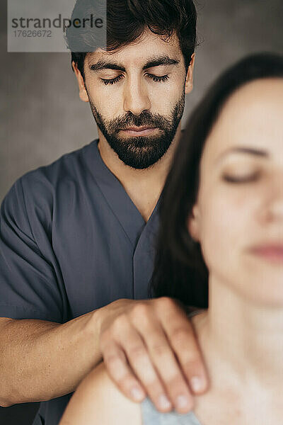 Physiotherapeut mit geschlossenen Augen massiert Frau auf der Schulter