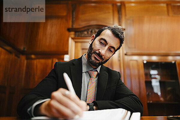 Selbstbewusster bärtiger männlicher Anwalt  der während einer Sitzung im Sitzungssaal ein Vertragsdokument unterzeichnet