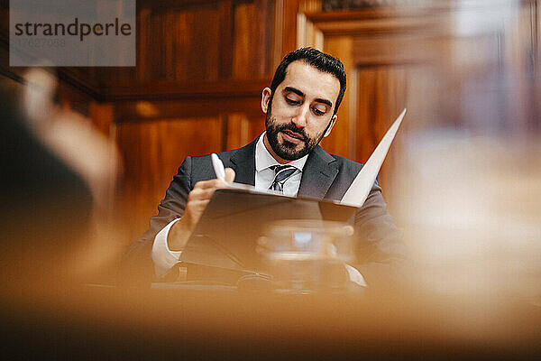 Selbstbewusster  bärtiger Geschäftsmann mit Vertragsunterlagen im Sitzungssaal während einer Sitzung