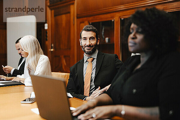 Porträt eines lächelnden Geschäftsmanns  der mit Kollegen in einem Konferenzraum sitzt