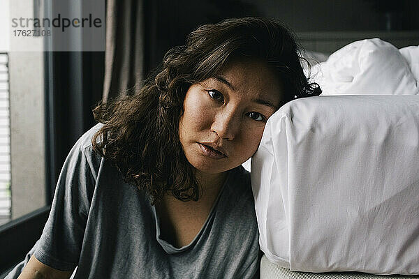 Porträt einer müden  einsamen Frau  die sich zu Hause ans Bett lehnt
