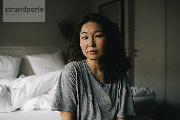 Porträt einer traurigen  psychisch kranken Frau  die zu Hause im Schlafzimmer sitzt