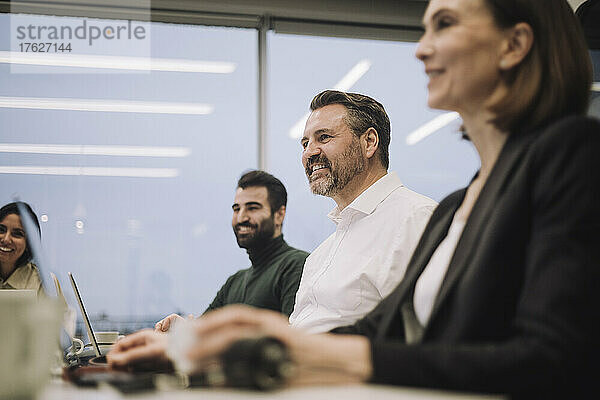 Lächelnde Geschäftsfrau mit männlichen und weiblichen Kollegen  die sich bei der Arbeit im Büro unterhalten