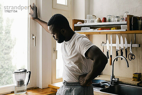 Depressiver einsamer Mann mit Hand auf der Hüfte in der Küche zu Hause stehend