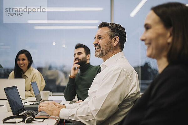 Lächelnder Geschäftsmann  der mit männlichen und weiblichen Kollegen während einer Besprechung im Büro diskutiert