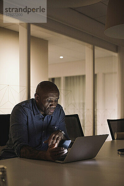 Älterer Geschäftsmann  der nachts im Büro an seinem Laptop arbeitet