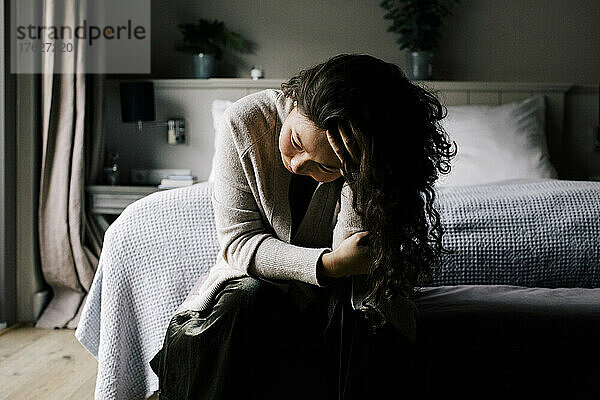 Emotional depressive Frau sitzt mit der Hand im Haar auf dem Bett zu Hause