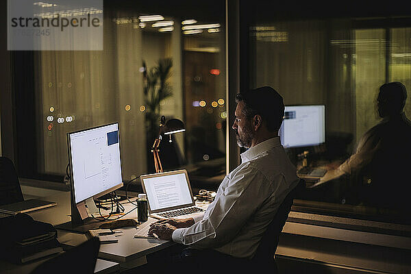 Geschäftsmann beim Tippen auf der Computertastatur während der Arbeit im Büro bei Nacht