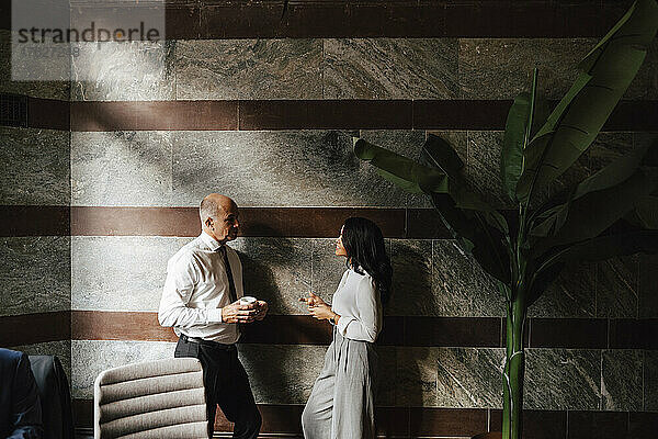 Geschäftsmann und Geschäftsfrau lehnen sich an die Wand  während sie in einer Anwaltskanzlei gemeinsam eine Strategie diskutieren