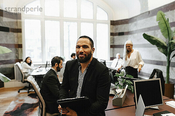 Porträt eines lächelnden  selbstbewussten männlichen Finanzberaters  der mit einem Dokument im Büro sitzt