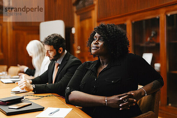 Selbstbewusste Geschäftsfrau mit verschränkten Händen  die während einer Sitzung am Konferenztisch im Sitzungssaal sitzt