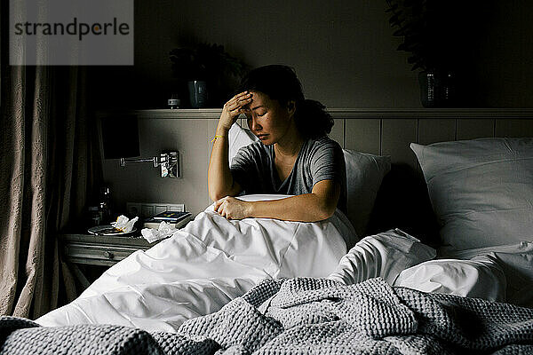 Psychisch depressive Frau sitzt mit dem Kopf in der Hand auf dem Bett zu Hause